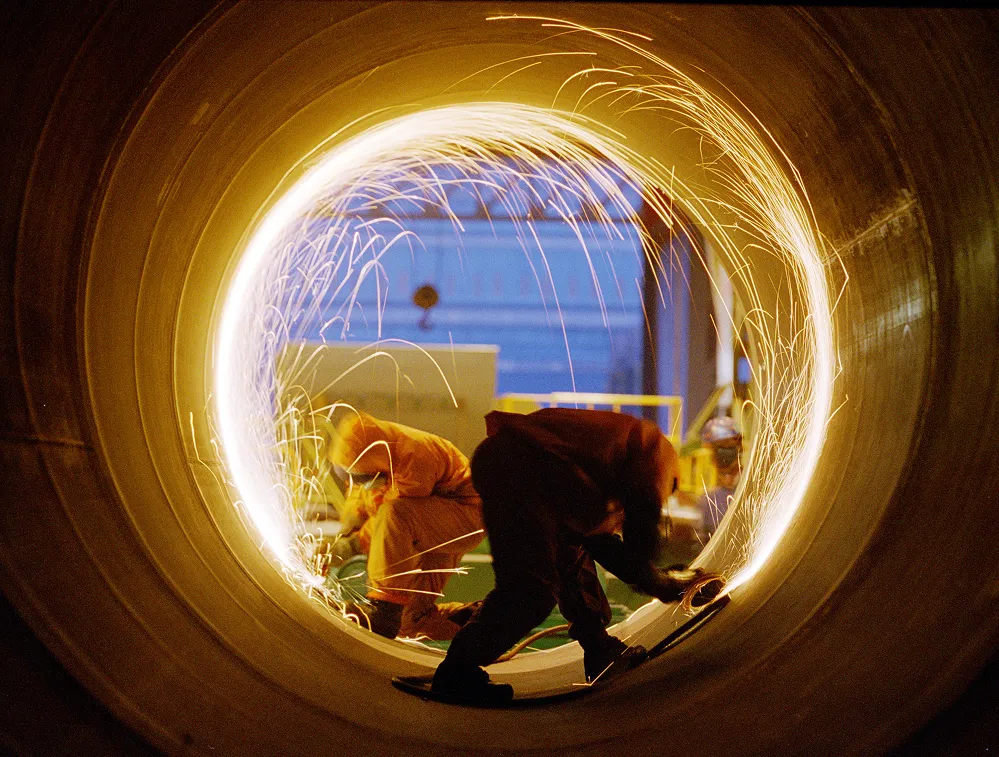 Hanwha Ocean workers conducting metalwork inside a large steel structure
