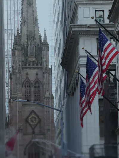 Historic building framed by tall city structures with U.S. flags lining the street in the foreground