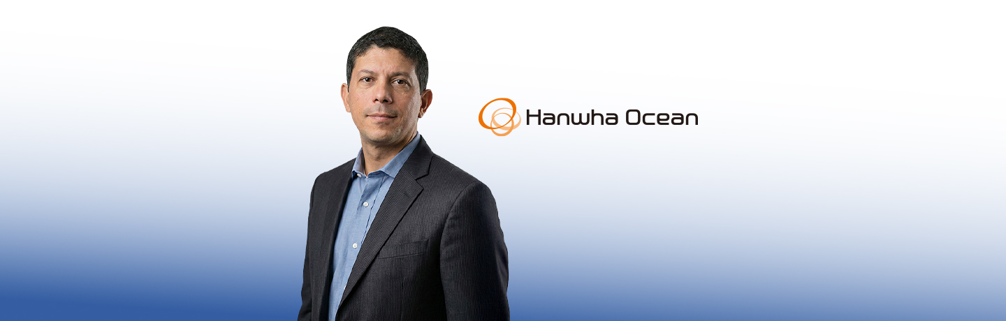 Weverton Nazario, Head of Operations and Maintenance at Hanwha Ocean, in a dark suit, standing against a gray wall  