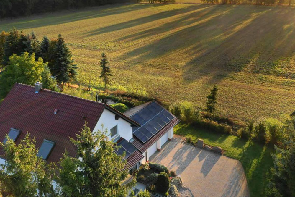 An aerial view of a house with Hanwha Qcells solar panels installed on the roof, with trees and a field nearby