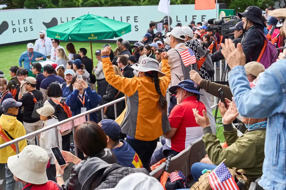 A Swedish golfer tees off in front of LIFEPLUS and Hanwha banners as spectators watch.