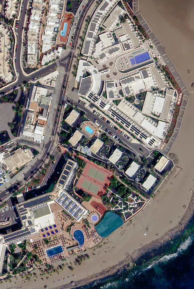 High-resolution satellite image of coastal buildings, pools, roads, and beachfront.
